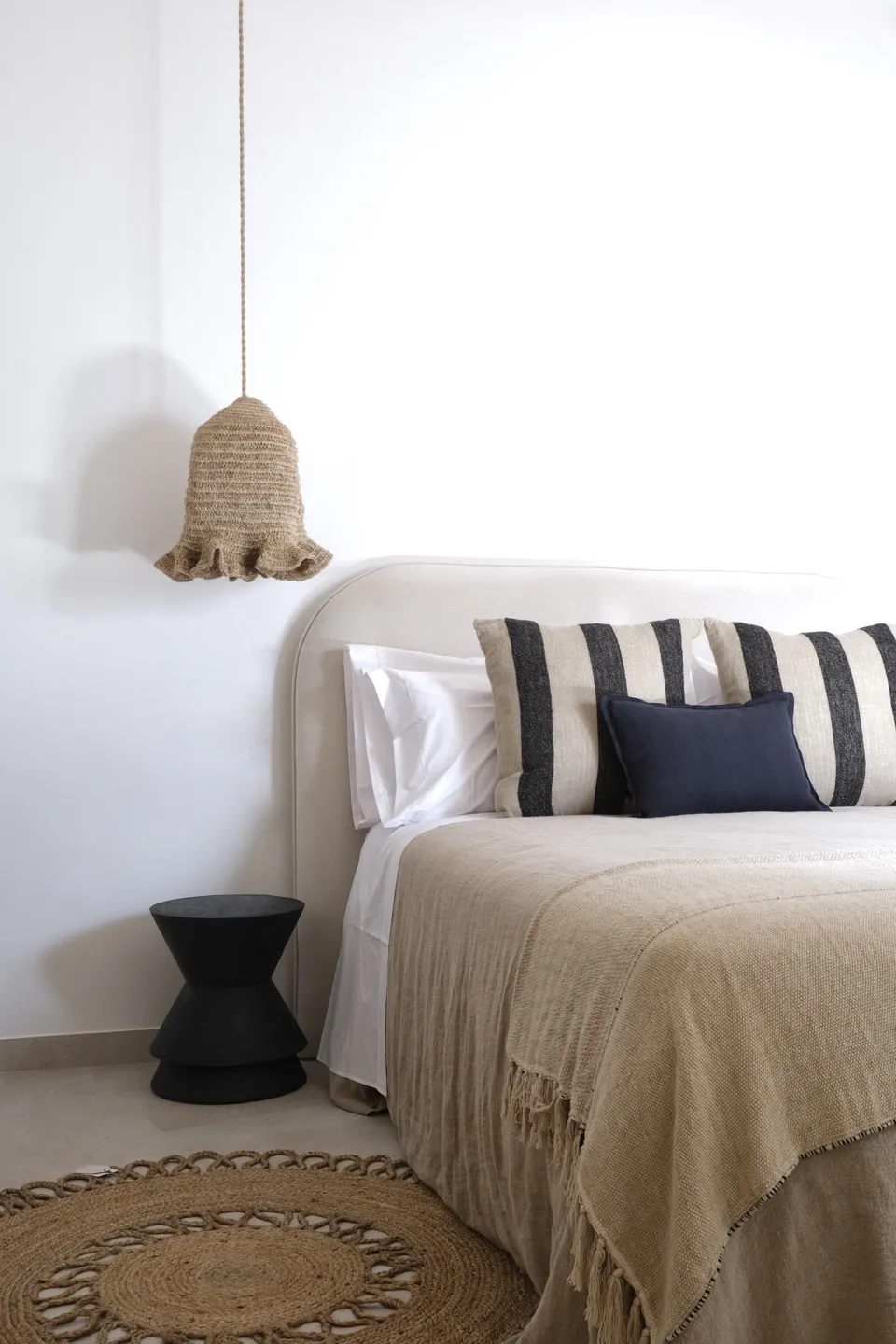 Paraíso — bed detail with linen throw, striped pillows, and jute pendant