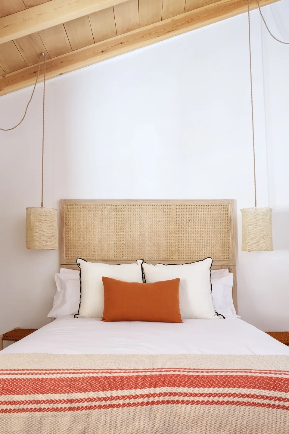 Paraíso — master bedroom with cane headboard, orange pillow, and rope pendants
